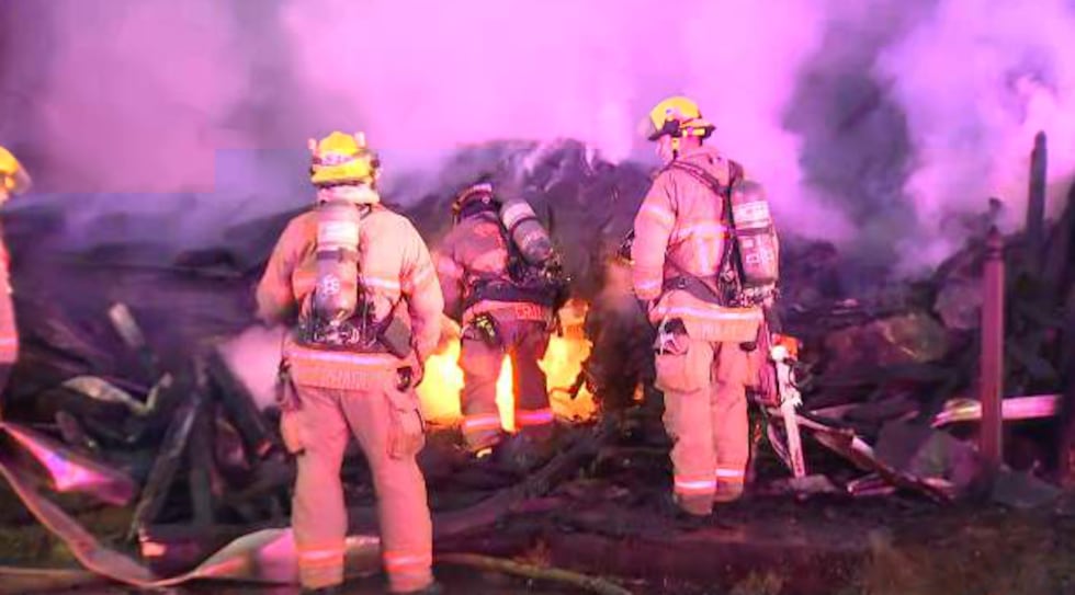 Firefighters stand over the remains of a house in Portland's Belmont neighborhood on Friday,...