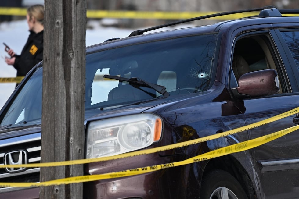 A bullet hole is seen in the windshield as law enforcement officers work at the scene of a...
